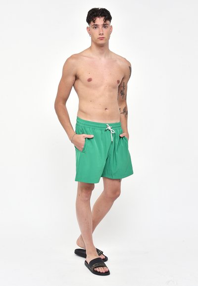 Costumi da bagno verdi realizzati in tessuto leggero. Presentano una vita elastica con cordino, tasche laterali e una texture liscia.