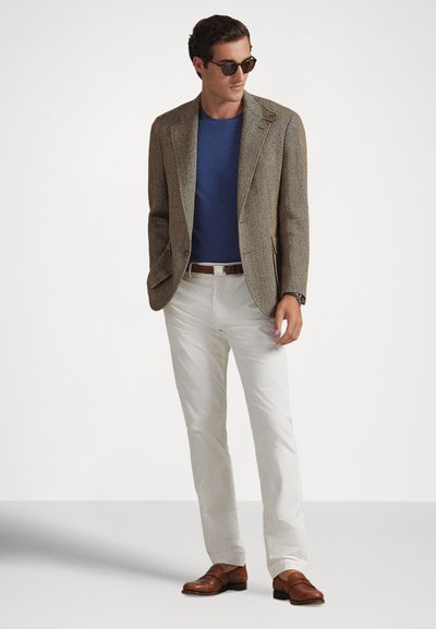 Καφέ σακάκι με ψαροκόκκαλο πάνω από μπλε μπλουζάκι με στρογγυλή λαιμόκοψη, λευκό στενό παντελόνι και καφέ μοκασίνια. Συμπληρώνεται με γυαλιά ηλίου και ρολόι χειρός.