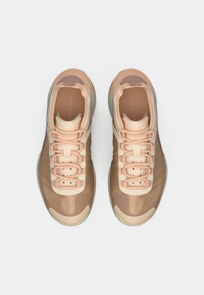 Scarpe da ginnastica beige con tomaia in mesh, dettagli traslucidi e suola leggera. I lacci passano attraverso sei anelli per una calzata sicura.