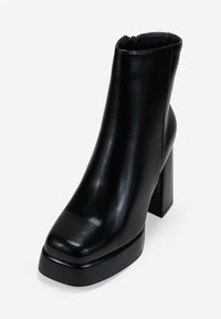 Botines negros hechos de cuero suave, con puntera cuadrada, tacón alto de bloque y cierre lateral con cremallera. Diseño minimalista y acabado elegante.