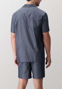 Set di camicia a maniche corte e pantaloni corti di colore navy realizzato in tessuto leggero. Presenta un piccolo motivo a pois bianchi e un colletto a punta.