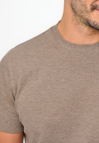 T-shirt in cotone marrone con scollatura a girocollo, maniche corte e una consistenza liscia, caratterizzata da dettagli di cucitura minimi attorno al collo.