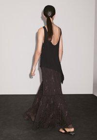 Black sleeveless top with an open back, layered over a dark patterned maxi skirt, featuring ruffled hem and lightweight fabric.