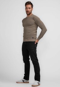 Beige ribbed long-sleeve sweater paired with black jeans and white sneakers featuring black accents. The fit is slim and casual.