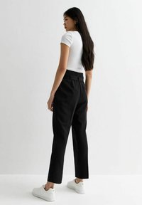 Svarta högmidjade byxor med rak bendesign, i kombination med en vit åtsittande t-shirt och vita sneakers. Slät tyg, minimalistisk stil.