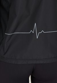 Schwarze Jacke mit einem weißen Herzschlaglinien-Graphic am Saum. Glattes, leichtes Material mit strukturierter Oberfläche.