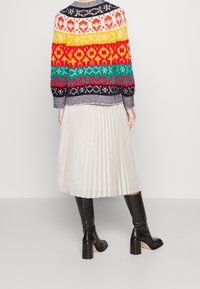 Suéter de punto con colores vibrantes y patrones en la parte de atrás, combinado con una falda plateada plisada y brillante y botas negras hasta la rodilla.