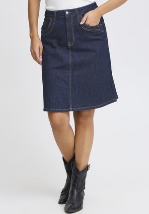 Denim skirt in dark wash with a straight cut, featuring front pockets and orange stitching. Paired with black cowboy boots.