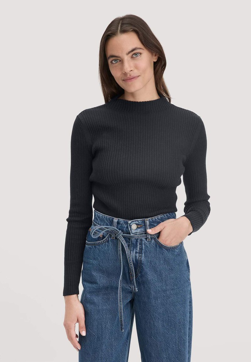 Schwarzes, geripptes Langarmshirt mit hohem Kragen, kombiniert mit hoch taillierten blauen Jeans aus Denim, die ein gebundenes Gürteldetail aufweisen.