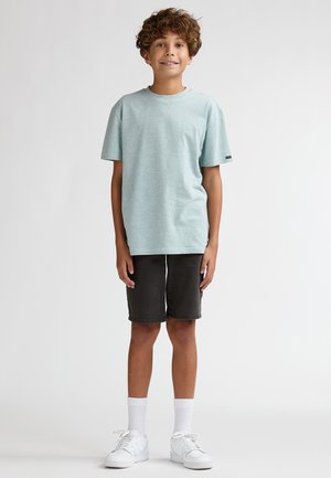 T-shirt rayé bleu clair à manches courtes, associé à un short gris foncé arrivant aux genoux. Des baskets blanches et des chaussettes montantes complètent la tenue.