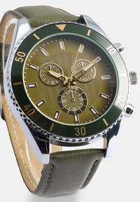 Vīriešu pulkstenis ar zaļu ādas siksnu, sudraba tonu korpusu, olīvu zaļu pulksteņa seju un zeltainiem akcentiem. Iespējas ietver trīs subdiales un teksturētu rakstu.