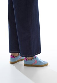 Sneakers in suede azzurro chiaro con dettagli rosa, dotati di una suola in gomma testurizzata e lacci piatti. Abbinate a pantaloni in denim scuro larghi.