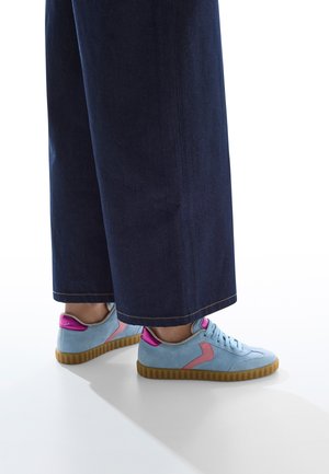 Sneakers in suede azzurro chiaro con dettagli rosa, dotati di una suola in gomma testurizzata e lacci piatti. Abbinate a pantaloni in denim scuro larghi.