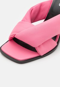 Gros plan d'une sandale rose avec des brides épaisses croisées rembourrées et un bout carré sur une semelle noire.