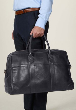 Black leather duffel bag with dual handles, rectangular shape, smooth texture, and vertical seams. Logo embossed on the front.