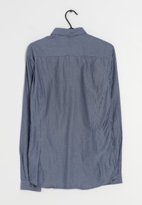 Camicia a maniche lunghe a righe verticali blu e bianche, con polsini a bottoni, colletto e design a schiena dritta. Appesa a un gancio.