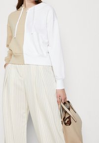 Felpa con cappuccio dallo stile color block beige e bianco. Presenta una vestibilità comoda e polsini a costine. Abbinata a pantaloni a righe crema.