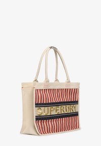 Canvas tote bag met een rood en beige gestreept design, voorzien van een zwarte streep en gouden "SUPERDRY" logo. Dubbele hengsels voor draaggemak.