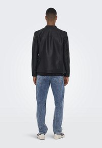 Zwart leren jack met een gladde textuur, voorzien van een rechte snit, staande kraag en subtiele details op het achterpaneel, gecombineerd met blauwe jeans.
