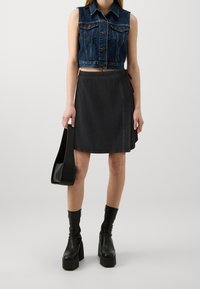 Chaleco de mezclilla con un diseño corto, falda envolvente negra, botas de plataforma negras y un bolso negro. Presenta botones y detalles de costura.