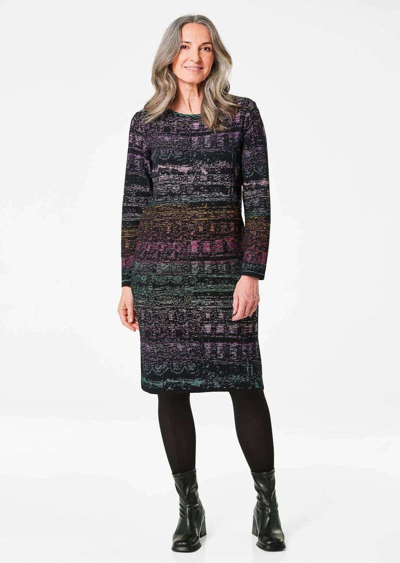 Robe longueur genoux avec des manches longues, présentant un motif texturé multicolore de violet, noir et vert. Portée avec des bottines noires.