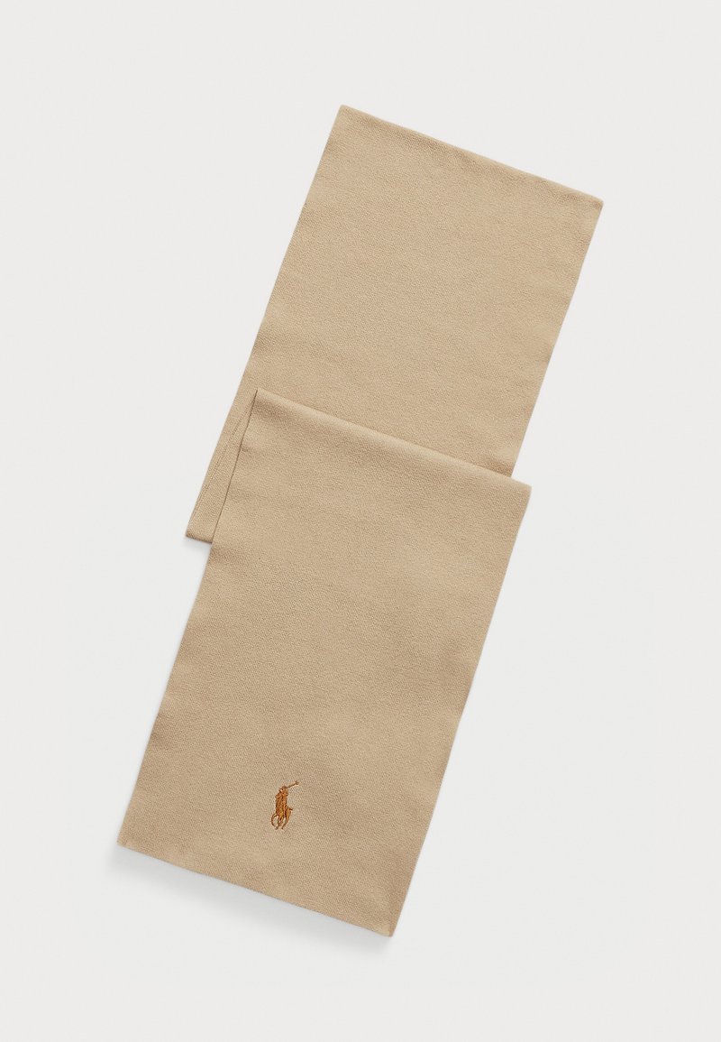 Beige skjerf laget av myk tekstil, med et enkelt design. Inkluderer en liten brodert logo i en kontrasterende farge nær bunnen.