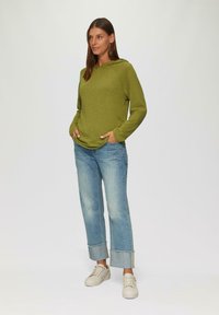 Grüne Kapuzenjacke, entspannter Schnitt, lange Ärmel, Taschen; kombiniert mit hellblauen, verkürzten Jeans mit umgeschlagenen Säumen und weißen Sneakern.