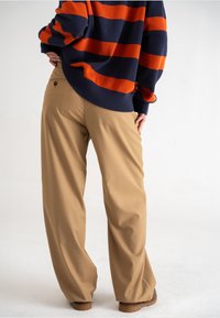 Tanden brede beenbroek met een gladde textuur, voorzien van een elastische tailleband en een achterzak, gecombineerd met een gestreepte marineblauwe en oranje trui.