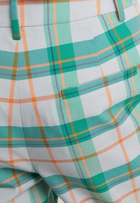 Spodnie w kratę z zielonymi, pomarańczowymi i fioletowymi wzorami na jasnoszarym tle, z detalem tylnej kieszeni. Tkany wzór.