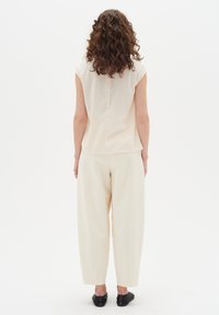 Light beige sleeveless top paired with loose cream trousers. Textured fabric and relaxed fit. Worn with simple black shoes.
