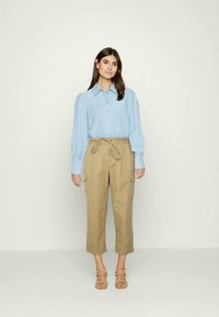 Camisa de botão azul claro com mangas longas, combinada com calças cargo beige encurtadas com cintura amarrada. Usada com sandálias castanhas.
