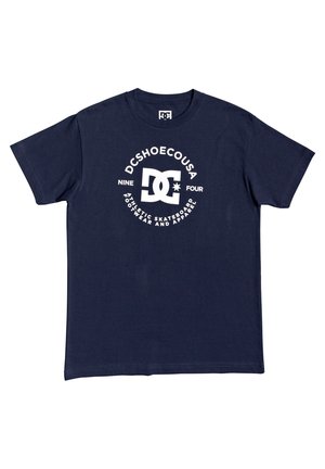Marineblå kortærmet t-shirt med hvid DC-logo og tekst "DCSHOECOUSA," "NINE FOUR," og "ATHLETIC SKATEBOARD FOOTWEAR AND APPAREL" på fronten.