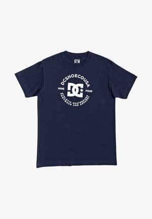 T-shirt blu navy a maniche corte con logo DC bianco e testo "DCSHOECOUSA," "NINE FOUR" e "ATHLETIC SKATEBOARD FOOTWEAR AND APPAREL" sul davanti.