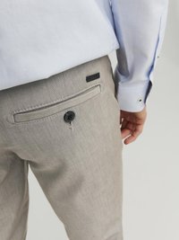 Pantalons gris clair avec une finition texturée, présentant un bouton noir et une poche arrière. Accompagnés d'une chemise bleu clair.