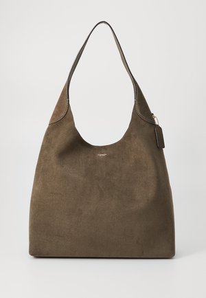 Sac bandoulière en daim marron avec une large bandoulière unique et un petit logo Coach centré sous l'ouverture, sur un fond uni.