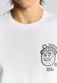 Weißes Baumwoll-T-Shirt mit einem schwarzen Sketch eines Bartes mit einem Hut und dem Text "HIGHLAND 1874" auf der linken Brustseite.