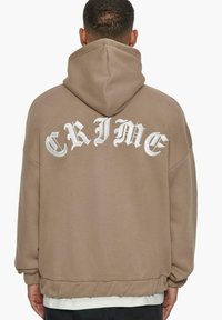 Hoodie marron à coupe surdimensionnée, avec un texte vertical blanc "CRIME" au dos. Fabriqué en tissu doux avec des poignets et un ourlet côtelés.