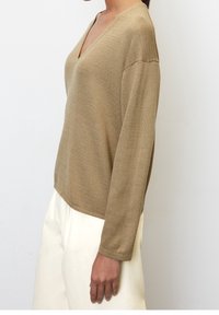 Maglione a maglia color marrone chiaro con scollo a V e maniche lunghe, caratterizzato da una vestibilità comoda e un tessuto strutturato, abbinato a pantaloni bianchi.