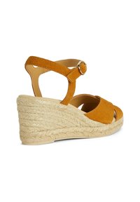 Sandalo con zeppa in suede color beige con piattaforma in juta intrecciata. Presenta una fascia alla caviglia con fibbia dorata e un design con punta aperta.