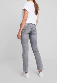 Jeans grises de corte slim, con un acabado desgastado y bolsillos traseros bordados, combinados con una camiseta blanca de mangas enrolladas y zapatillas blancas.