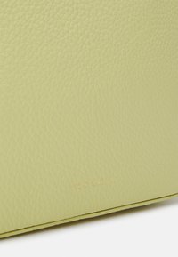 Borsa in pelle verde texture con logo 'Coccinelle' embossato in una sottile tonalità dorata, con bordi puliti e design minimalista.