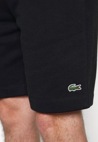 I pantaloni corti neri in cotone presentano una silhouette aderente, una texture liscia e un piccolo logo di coccodrillo verde sull'orlo inferiore sinistro.