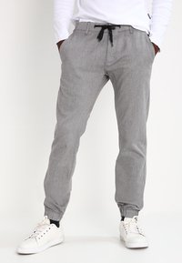 Pantalons grisés fuselés avec une finition texturée, des poignets élastiqués et une taille à cordon, associés à des baskets blanches.