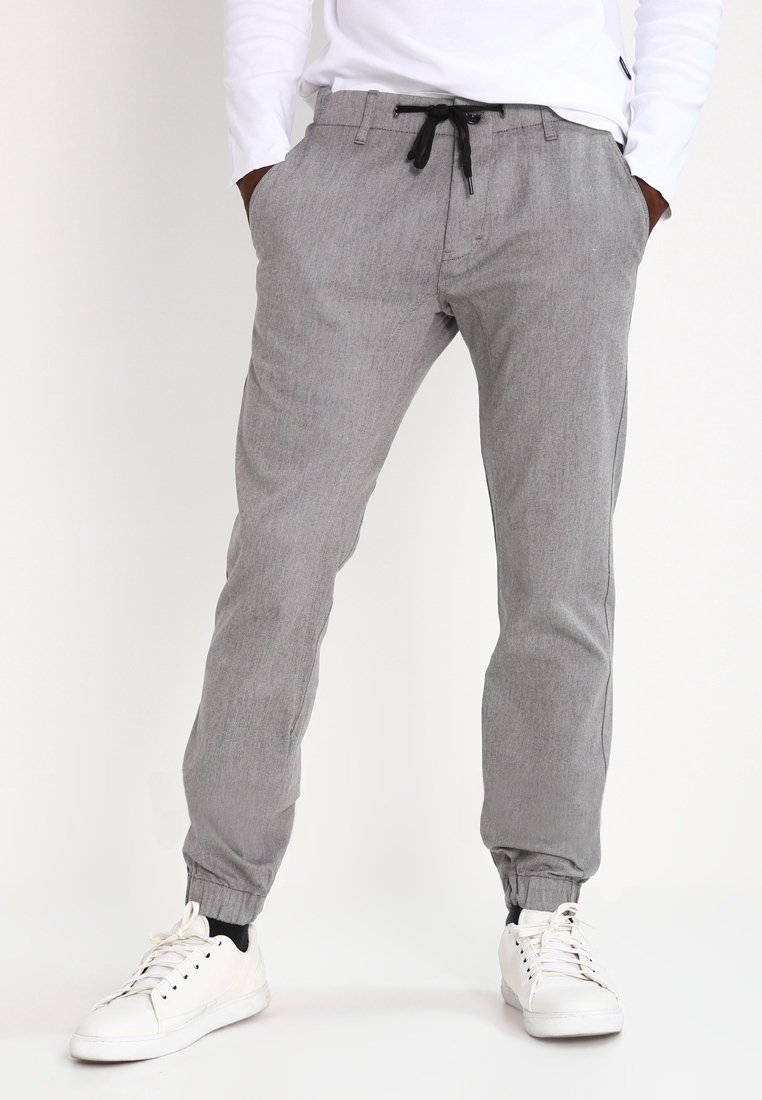 Pantalons grisés fuselés avec une finition texturée, des poignets élastiqués et une taille à cordon, associés à des baskets blanches.