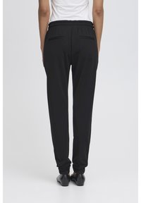 Svart joggebukse med elastisk midje, som har to baklommer og smale mansjetter. Laget av myk, elastisk stoff for komfort.