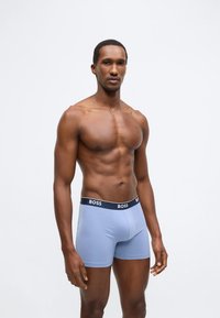 Kék férfi boxeralsó, testhez simuló szabással és fekete derékpánttal, amelyen a "BOSS" logó látható. Az anyag sima és könnyű hatású.