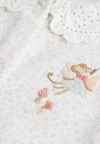 White fabric with pink speckles, featuring a lace collar and embroidered design of a mouse with mushrooms. Snap buttons on placket.