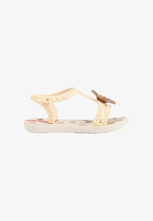 Sandalo per bambino color crema con cinturini intrecciati, plantare stampato con motivi floreali e decorazione a fiore marrone sulla fascia frontale.