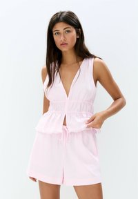 Top roz fără mâneci, cu decolteu adânc în V, talie elastică și margine desfăcută; asortat cu pantaloni scurți matching, cu șnur și croială lejeră.