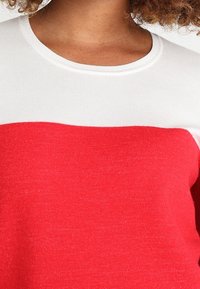 Suéter bloqueado en rojo y blanco, con un cuello redondo y una textura de punto suave. La mitad superior es blanca, mientras que la mitad inferior es de un vibrante color rojo.